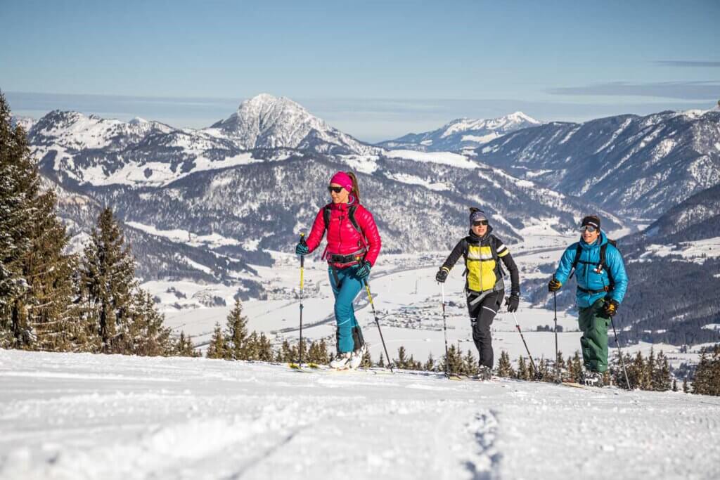 Wintersportler wandern durch die verschneite Tiroler Landschaft mit Bergen im Hintergrund.