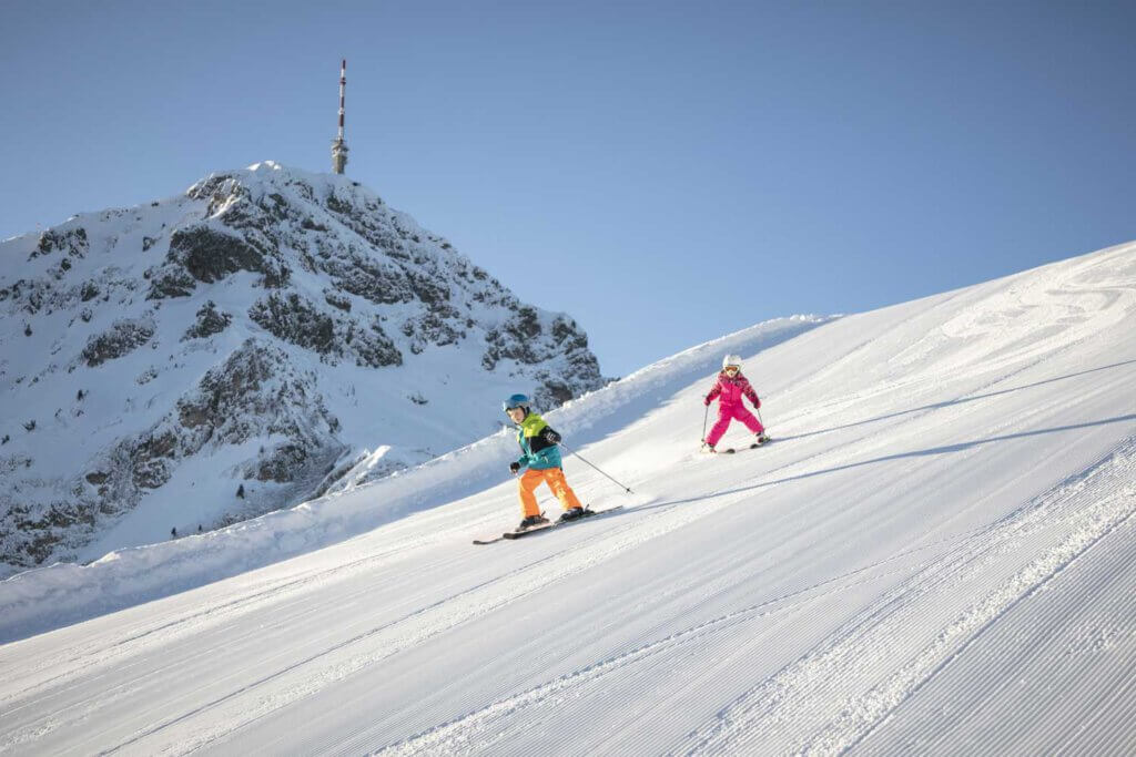 Kinder beim Skifahren in den Tiroler Alpen mit schneebedeckten Pisten und Berggipfel.