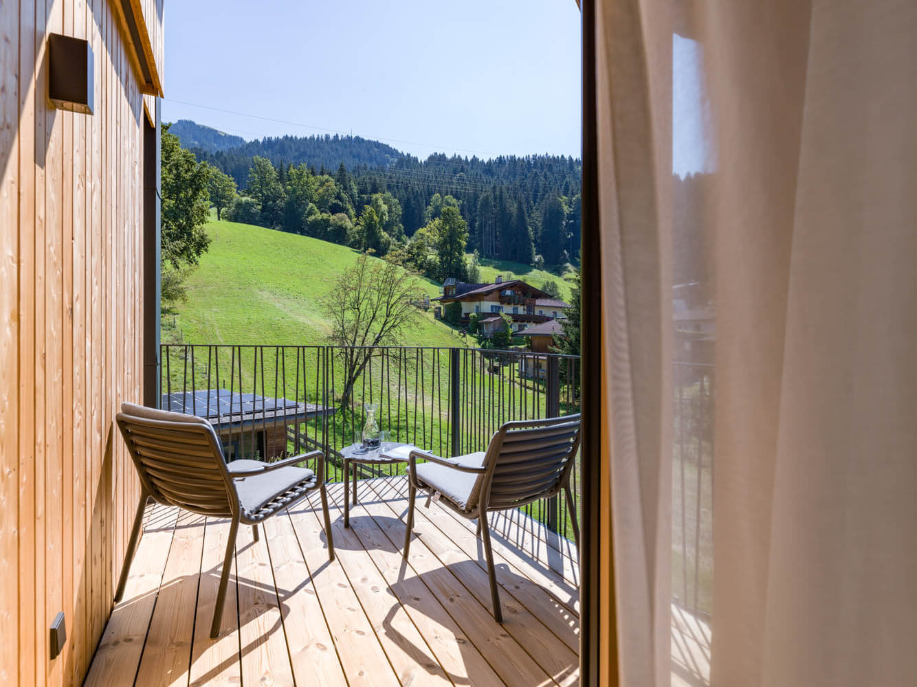 Balkon mit Stühlen, Blick auf grüne Wiesen und die Tiroler Berge im Hintergrund.