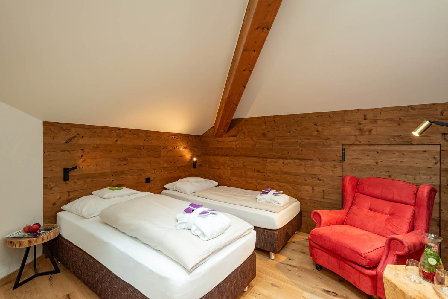 Gemütliches Zimmer im Hotel Penzinghof mit zwei Betten und rotem Sessel in Tiroler Holzdecor.